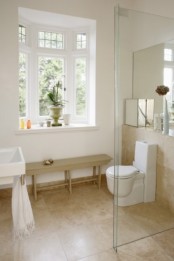 a neutral bathroom with a tan tile floor, a tan bench and white appliances and a shower space enclosed in glass