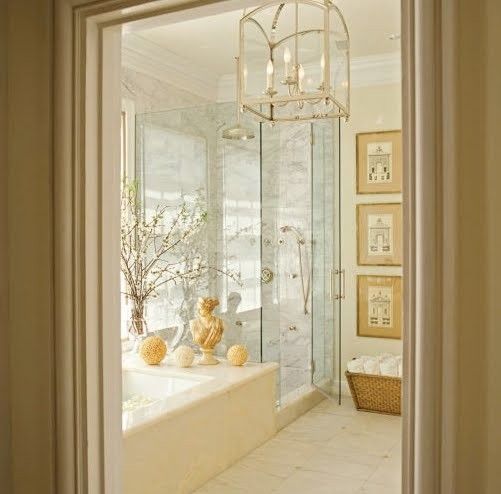 a neutral bathroom with a built-in tub clad with marble, a shower space, a gallery wall and a vintage chandelier