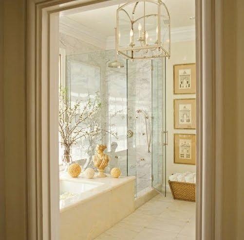 a neutral bathroom with a built-in tub clad with marble, a shower space, a gallery wall and a vintage chandelier