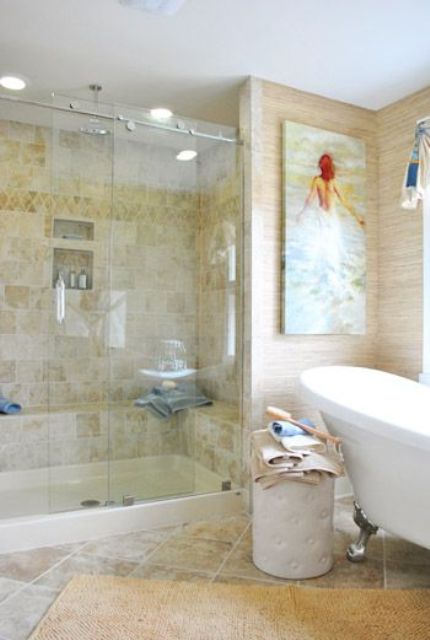 a tan-colored bathroom clad with tiles, with neutral wallpaper, a vintage bathtub and a shower space plus a bold artwork