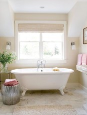 a welcoming warm-colored bathroom with tan walls, a clawfoot tub and a shiny metallic side table plus pink towels