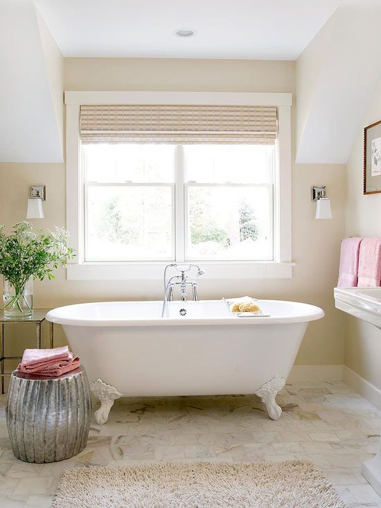 a welcoming warm-colored bathroom with tan walls, a clawfoot tub and a shiny metallic side table plus pink towels