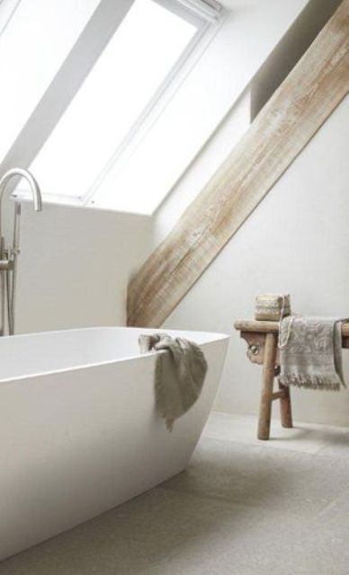 a neutral minimalist attic bathroom with rough wooden beams and a rough wooden bench, neutral towels and a lovely bathtub is amazing