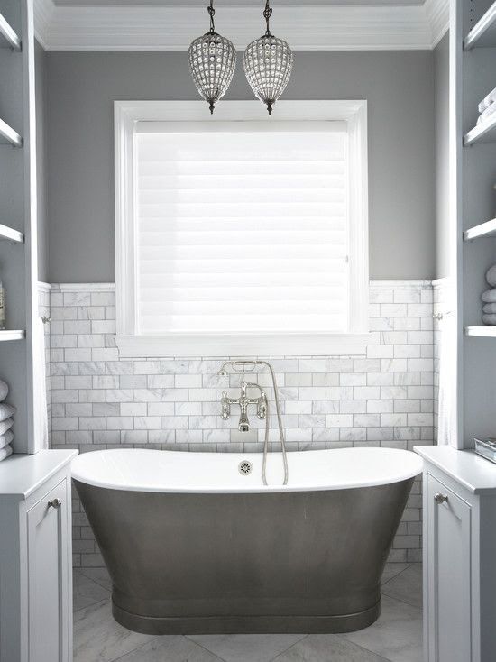a small and chic grey and white bathroom with marble tiles, a free-standing tub and built-in shelves