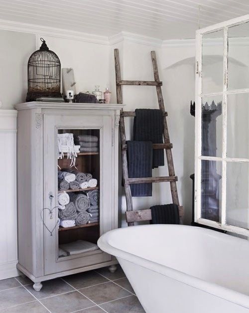 a Scandinavian bathroom with a ladder, a glass armoire with towels, a cage and a bathtub with a glass space divider