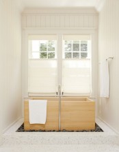 a neutral bathroom with a wood ofuro tub by the windows with shades placed into pebbles