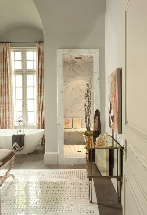 a refined and luxurious neutral bathroom clad with marble and marble tiles, an oval tub, vintage furniture and printed textiles