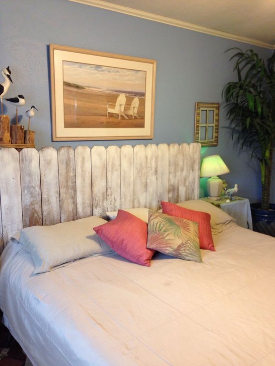 a bedroom with blue walls, a bed with a whitewashed headboard, artwork and a potted statement plant is cool