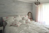 a shabby chic bedroom with a whitewashed headboard that is extended up to the ceiling for a statement, a bed with floral bedding and a crystal chandelier