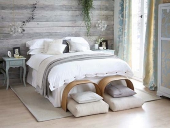 an airy bedroom with a shabby chic whitewashed headboard, a bed with neutral bedding, a couple of benches and pillows, vintage nightstands