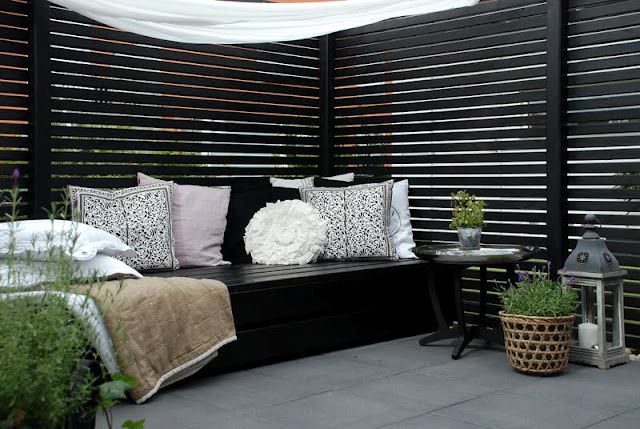 a moody Scandinavian terrace with black planked space dividers, a black bench with lots of pillows, potted greenery and blankets