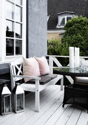 a laconic Scandinavian terrace with a white planked bench with pastel pillows, a black round table and some candle lanterns is a lovely idea