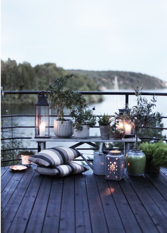 a Scandi terrace with a lake view, a bench with potted plants and candle lanterns, striped pillows is a lovely space with a gorgeous scenery around