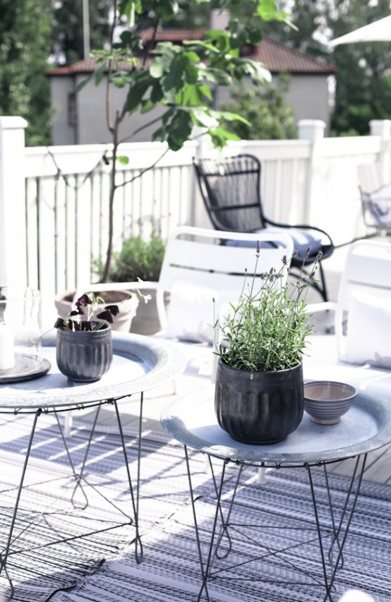 a Scandinavian terrace with metal side tables, white and black chairs, printed rugs and potted greenery and blooms