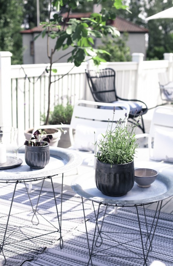 a Scandinavian terrace with metal side tables, white and black chairs, printed rugs and potted greenery and blooms a Scandinavian terrace with metal side tables, white and black chairs, printed rugs and potted greenery and blooms