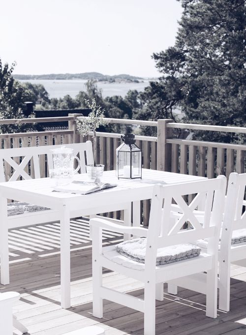 a simple Nordic terrace with a lake view, with white outdoor furniture, a candle lantern and some greenery around a simple Nordic terrace with a lake view, with white outdoor furniture, a candle lantern and some greenery around
