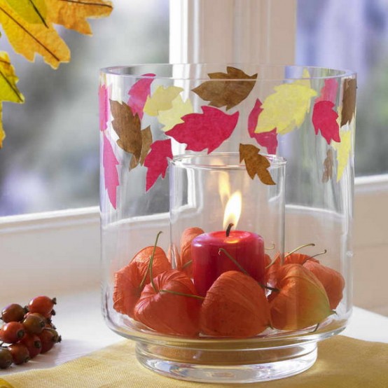 a large glass with seed pods and colorful paper leaves attached plus a colored candle inside is a lovely decoration for fall or Thanksgiving
