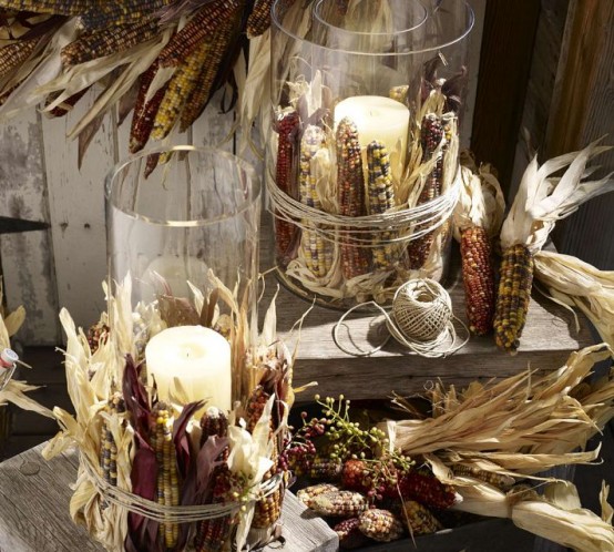 tall glass candleholders with pillar candles wrapped corn cobs and with corn husks are a pretty and cozy fall or Thanksgiving decoration you can easily make