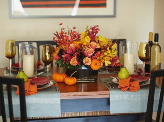 pillar candles accenting a bright floral Thanksgiving centerpiece creat e acozy ambience and invite everyone to the table