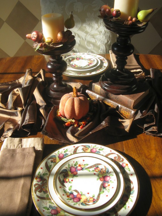 a vintage rustic Thanksgiving centerpiece of dark stained candleholders, faux apples and pears and pillar candles plus a brown table runner and pumpkins