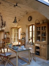 a rustic Provence dining space with an arched ceiling, a stained storage unit, a dining table, folding chairs, a metal pendant lamp and a crystal chandelier