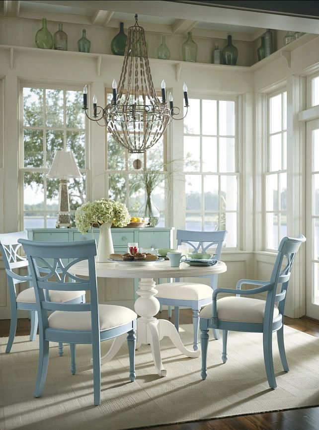 a vintage neutral and pastel sunroom with glazed walls, a white round table and powder blue chairs and an aqua sideboard plus bottles on display