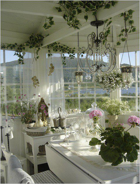 a charming neutral sunroom with crystal chandeliers and lamps, with potted blooms and greenery and a lovely view