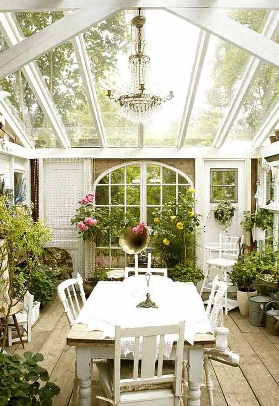 an elegant vintage sunroom with a glazed ceiling, white vintage furniture, a crystal chandelier, potted greenery and blooms looks refined