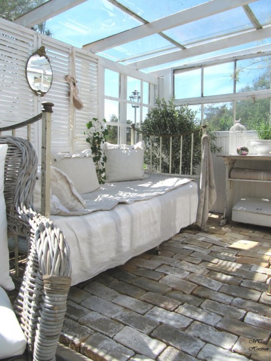 a vintage white sunroom with shutters, neutral forged and wicker furniture, potted greenery and a cage for decor