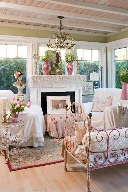 a refined vintage sunroom in neutrals and pastels, with a non-working fireplace, a crystal chandelier, floral textiles, blooms in pots and vases and gorgeous views