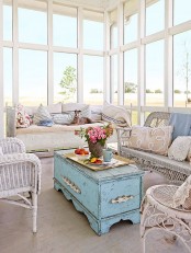 a vintage sunroom with all glazed walls, white wicker furniture, a blue shabby chic chest, printed and embroidered pillows and blooms in a vase