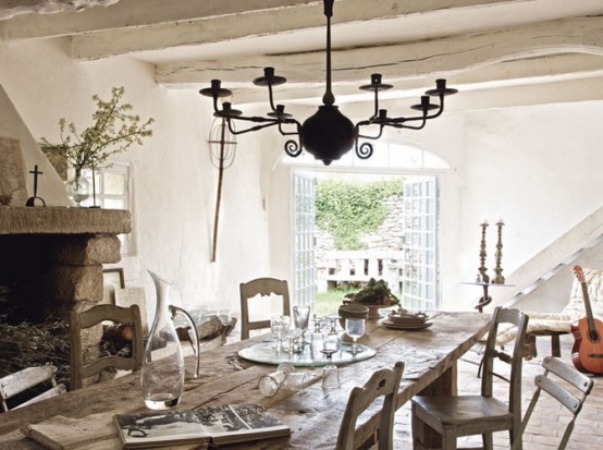 a French chic rustic dining room with a large heart clad with stone, a stained table and vintage chairs, a chic vintage chandelier and French doors to the garden