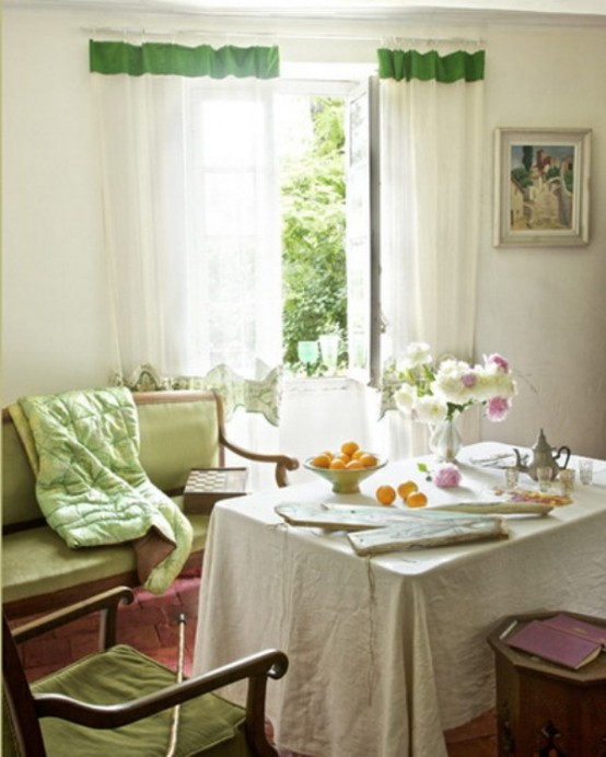 a neutral dining room with beautiful vintage furniture, a green loveseat and a chair, a vintage chair, a table and some curtains with green touches