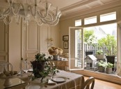 a beautiful neutral French dining room with paneling, a table and chic vintage chairs, a beautiful chandelier and a large window to enjoy the views