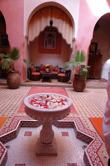 a pink and red Moroccan patio with dark carved furniture, a fountain and tiles all over