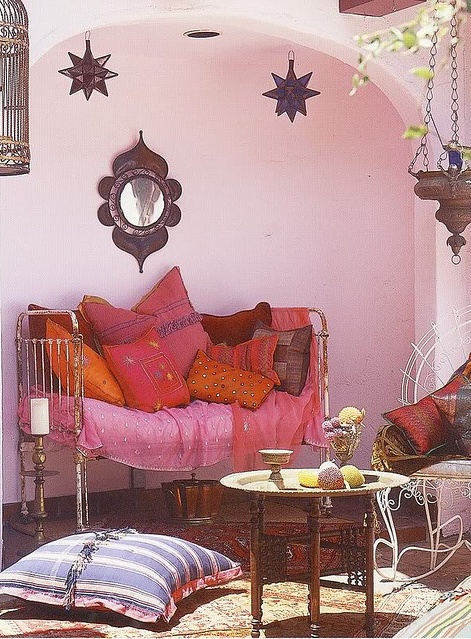 a pink Moroccan patio with bright textiles in pink, red and orange, low carved furniture and star lamps