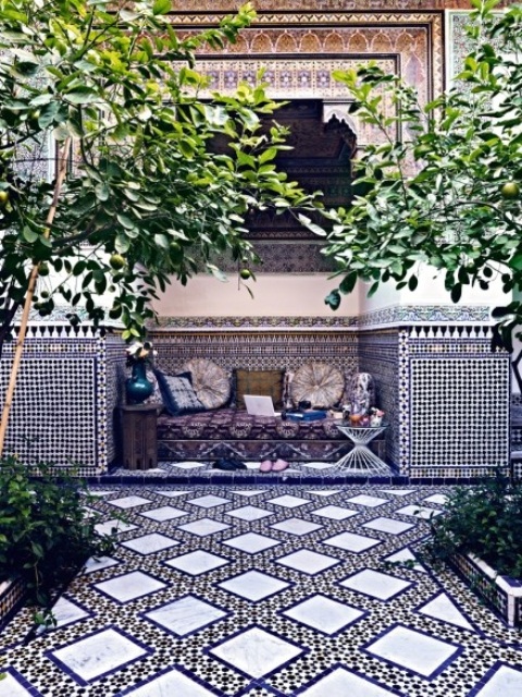 a welcoming Moroccan patio done with navy and white tiles, a dark upholstered bench and bright pillows