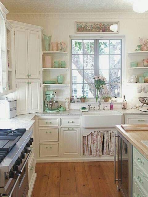 a romantic vintage and shabby chic kitchen with white cabinets, a floral cover under the sink, an aqua kitchen island and other aqua touches