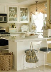 a neutral shabby chic kitchen with white cabinets, neutral tiles, a white kitchen island and a printed curtain plus white metal chairs with leather seats