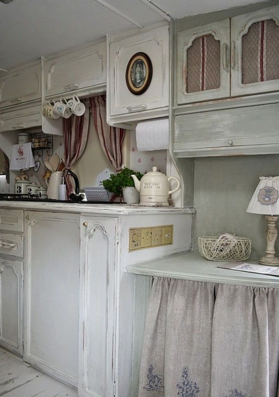 a neutral and pastel shabby chic kitchen with white cabinets, an olive green upper cabinet and a table, printed linens