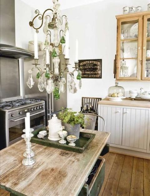 a charming farmhouse shabby chic kitchen with neutral cabinets, wooden glass ones, a crystal chandelier and a rustic kitchen island