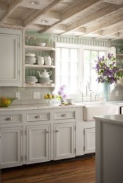 a charming white shabby chic kitchen with farmhouse cabinets, wooden beams on the ceiling, an aqua wall for a touch of color