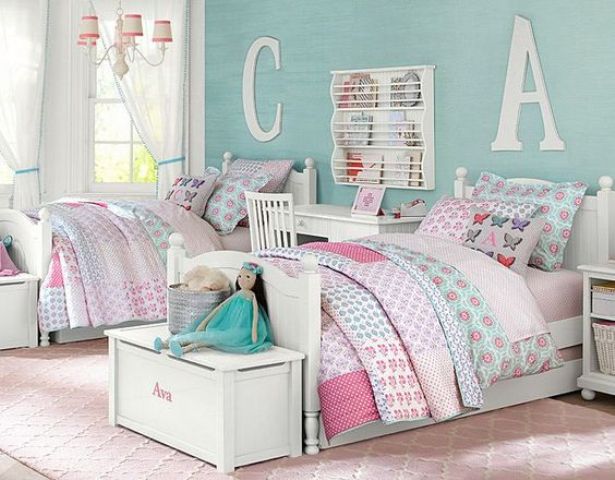 a pastel shared girls' bedroom with a turquoise accent wall, white vintage furniture, white chests for storage and nightstands, floral printed bedding and pillows