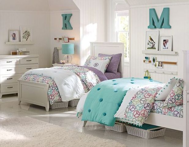a white shared girls' bedroom with white vintage furniture, colorful printed bedding, gallery walls and white baskets for storage under the beds