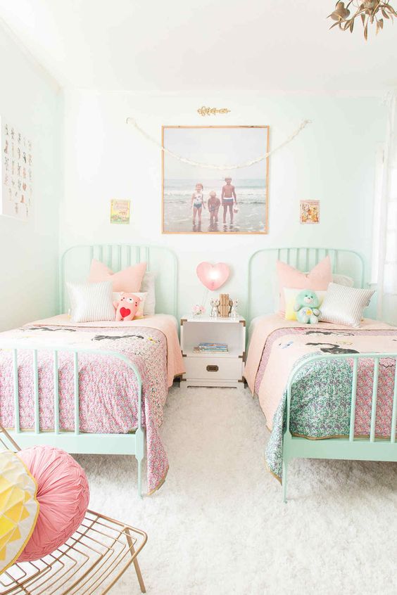 a white shared girls' bedroom with mint beds and pink and mint bedding, a gallery wall, a white nightstand, a gold chair with bright pillows a white shared girls' bedroom with mint beds and pink and mint bedding, a gallery wall, a white nightstand, a gold chair with bright pillows