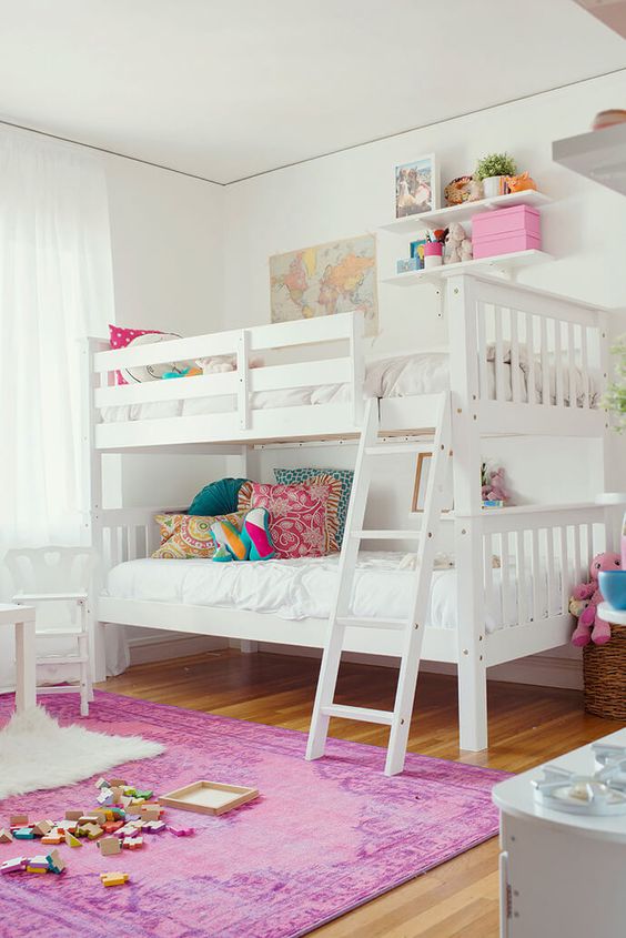 a stylish white shared girls' bedroom with a bunk bed, colorful pillows, white stools, a hot pink printed rug, colorful toys, decor and details