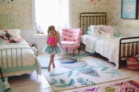 a bright and fun shared girls’ bedroom with mismatching metal beds, white vintage bedding, colorful rugs, bright pompom mobiles and toys