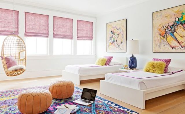 a chic shared girls' bedroom with a series of windows with pink curtains, contemporary beds, bright artworks, a colorful rug and orange leather poufs