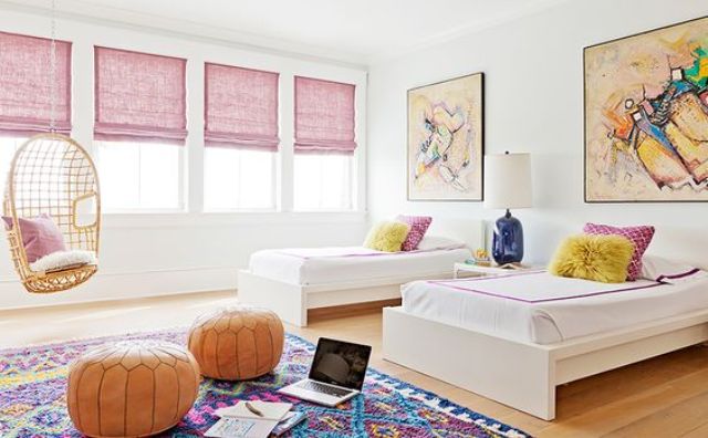 a chic shared girls' bedroom with a series of windows with pink curtains, contemporary beds, bright artworks, a colorful rug and orange leather poufs a chic shared girls' bedroom with a series of windows with pink curtains, contemporary beds, bright artworks, a colorful rug and orange leather poufs