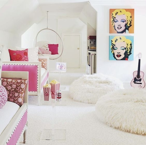 a pop art inspired white girls' bedroom with daybeds, bright artworks, open shelves, fluffy poufs and touches of bold pink and turquoise
